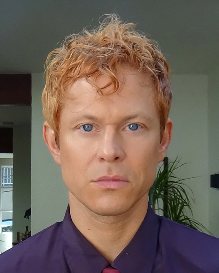 Close up portrait of Mike Hadreas making eye contact with the camera in a purple button up shirt and maroon tie